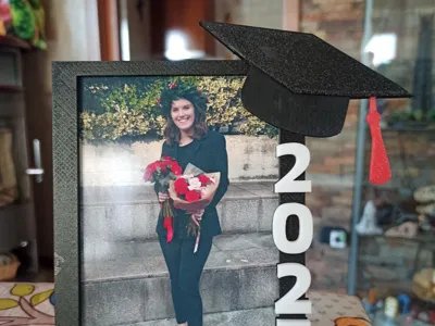 3D-printed graduation keepsake photo frame with a black mortarboard cap, red tassel and embossed year beside a graduate's photo